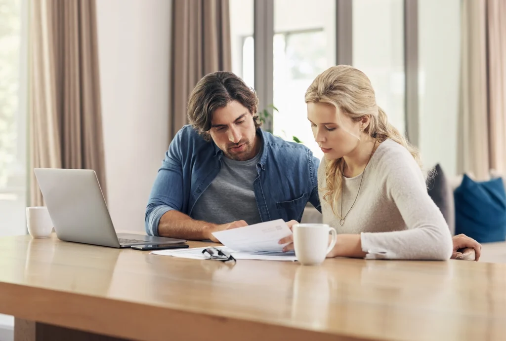 couple sitting down at table with computer, looking at insurance and financial documents