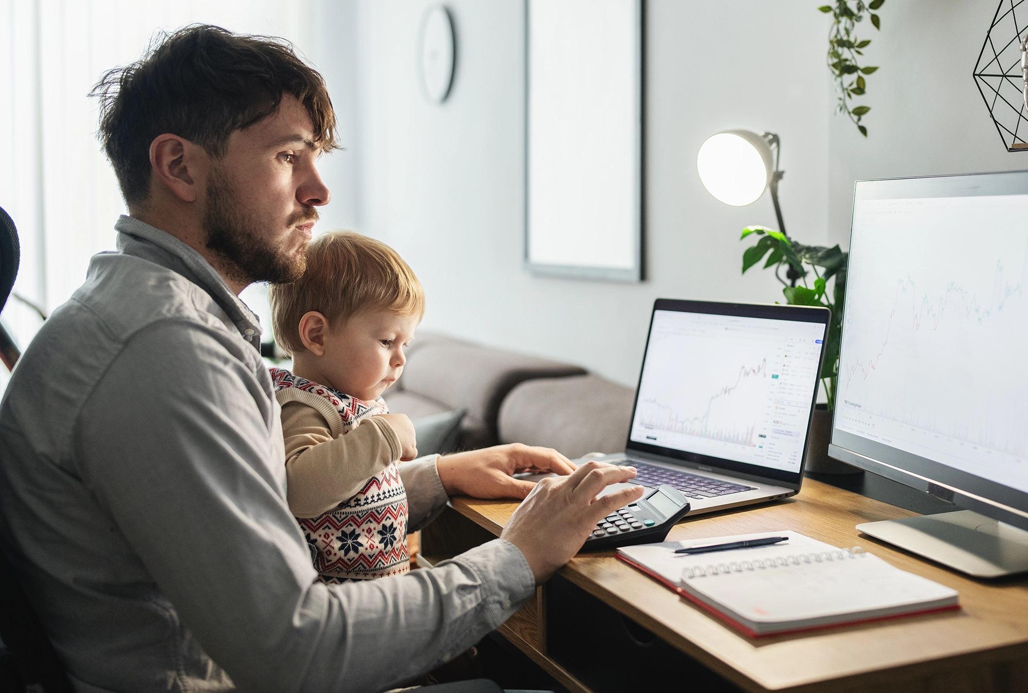 Image of man sitting at his computer with a child in his lap, looking at finances a computer